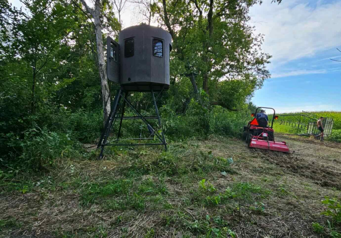 A man on a tractor with a tree stand in the background.